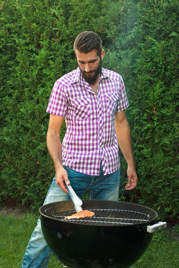 Junger Mann grillt Lachsforellen Filet im Garten