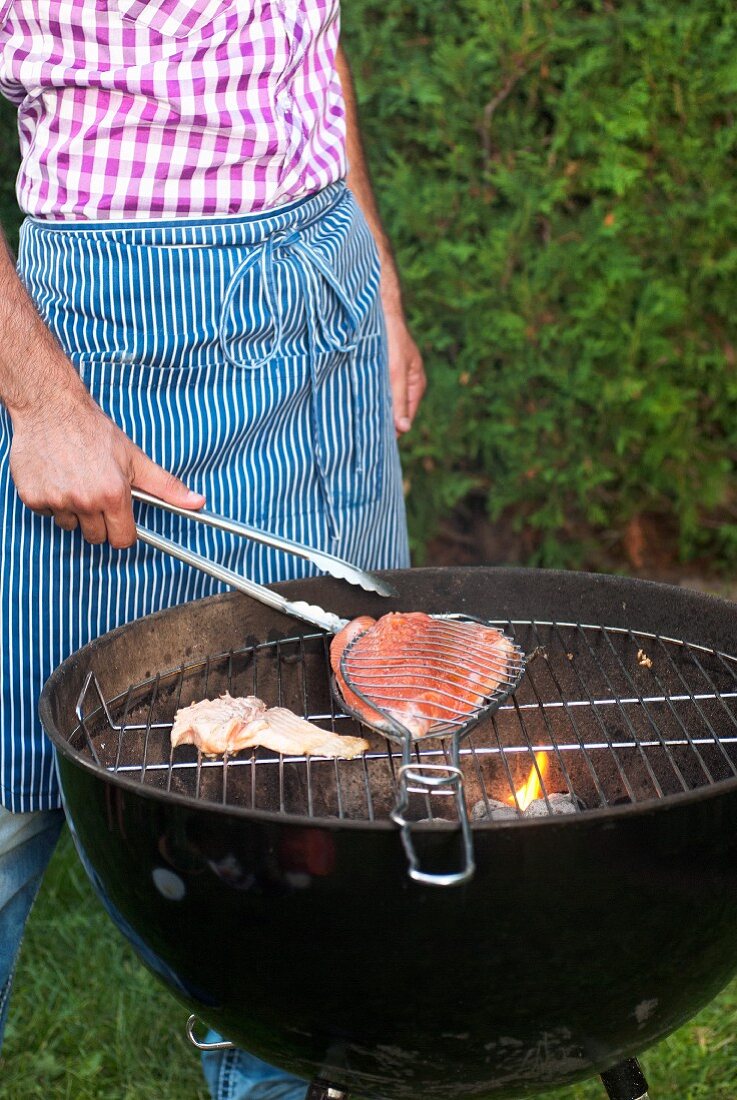 A man turning salmon fillets on a kettle barbecue