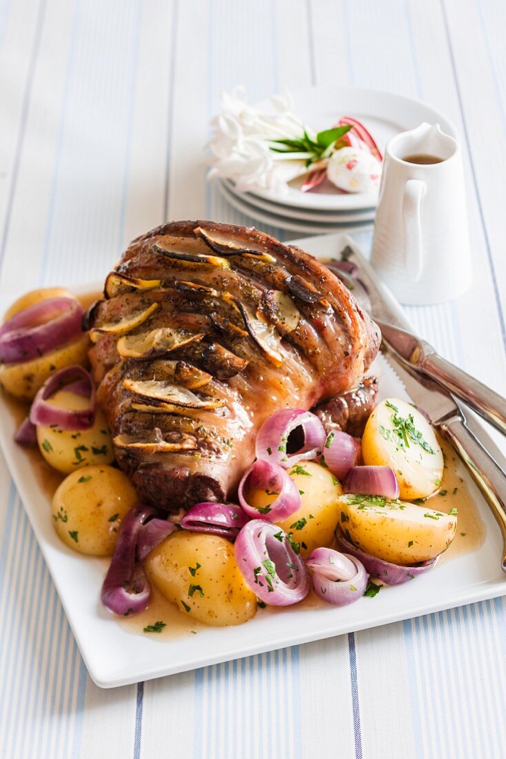 Roast lamb studded with lemons on a bed on potatoes and onions