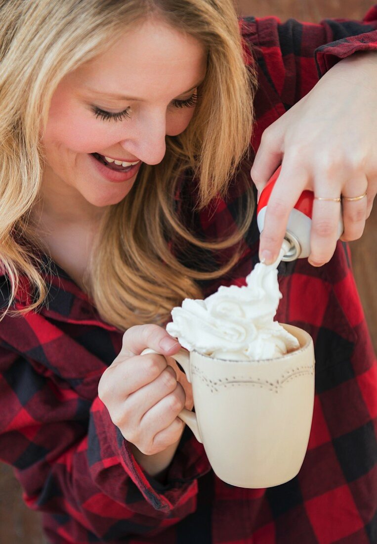 A young woman squirting cream onto a cup of hot chocolate
