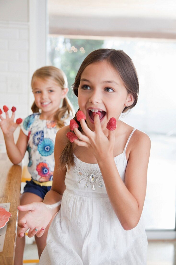 Zwei Schwestern mit Himbeeren auf ihren Fingern in der Küche