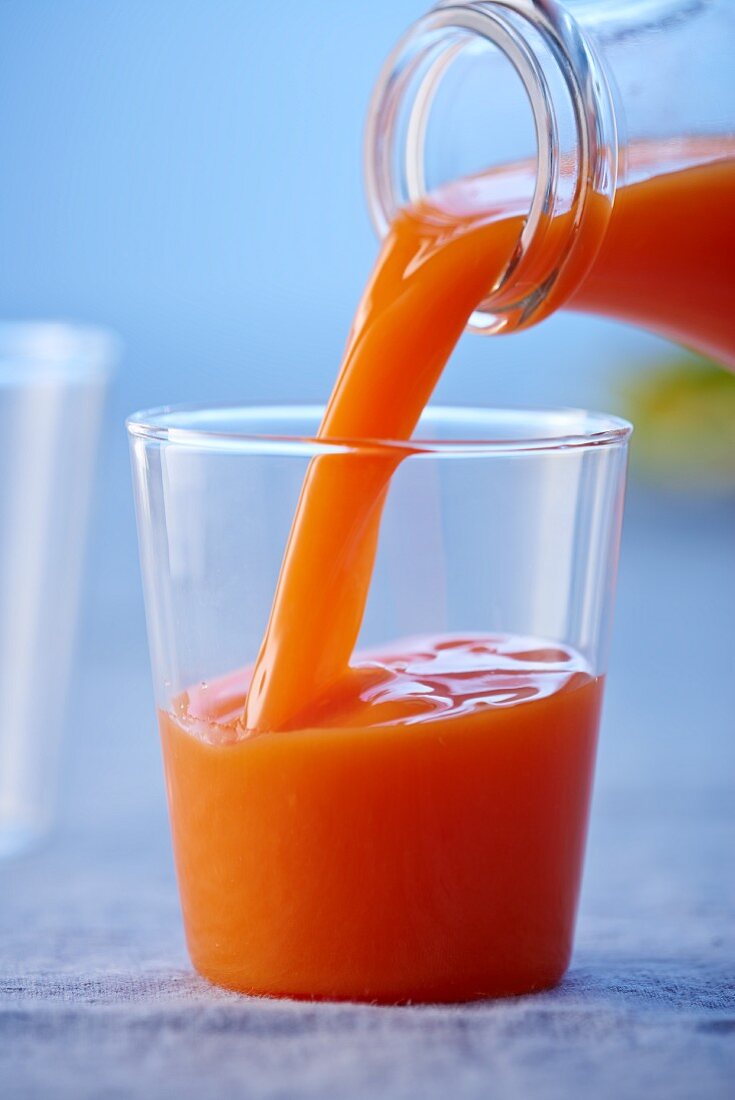 Orange and carrot juice being poured from a bottle into a glass