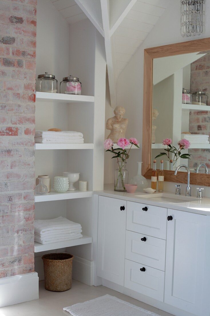 White fitted shelving and custom-made washstand below framed mirror on wall in corner of bathroom