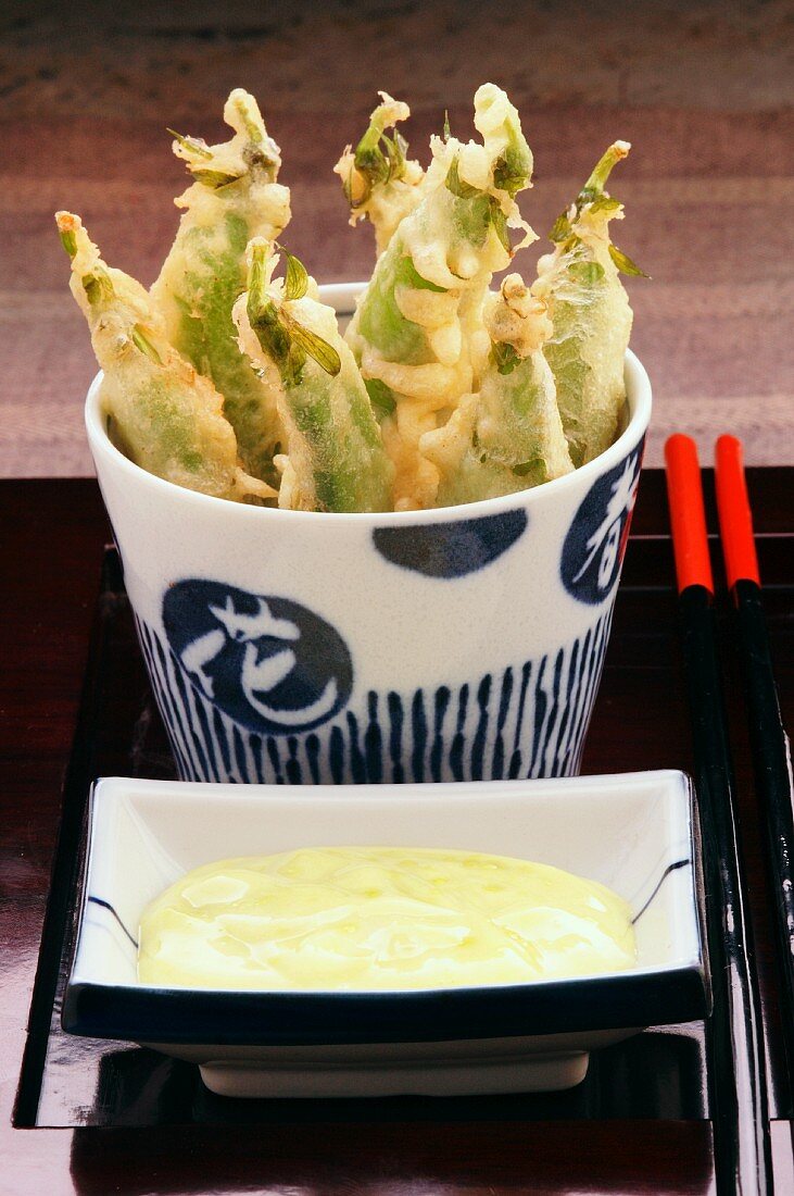 Pea pod tempura with a dipping sauce served in oriental crockery