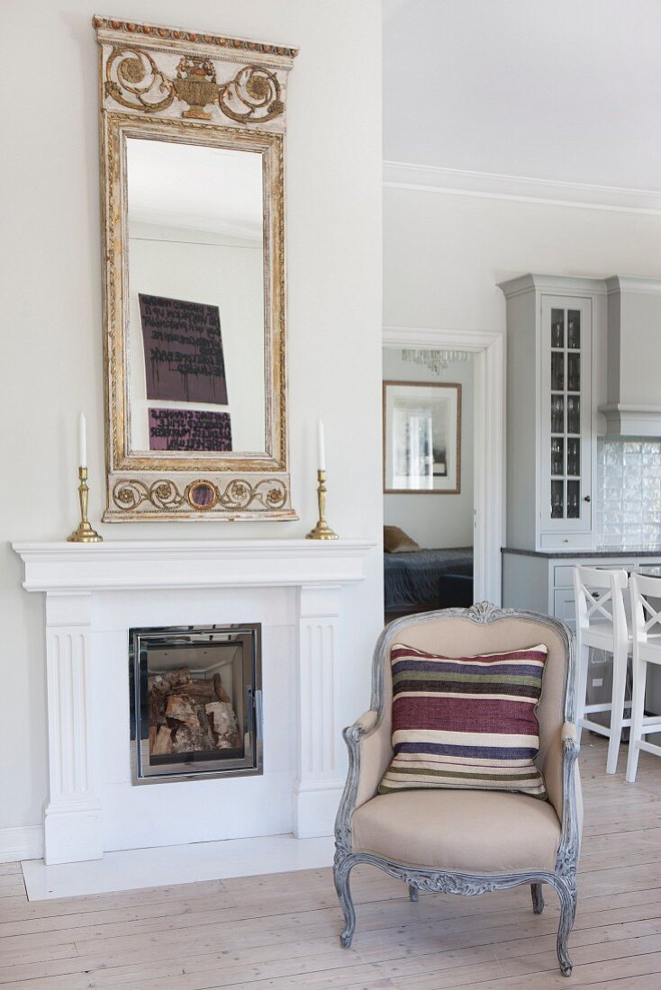 Striped scatter cushions on Rococo-style armchair in front of open fireplace with gilt-framed mirror on mantelpiece