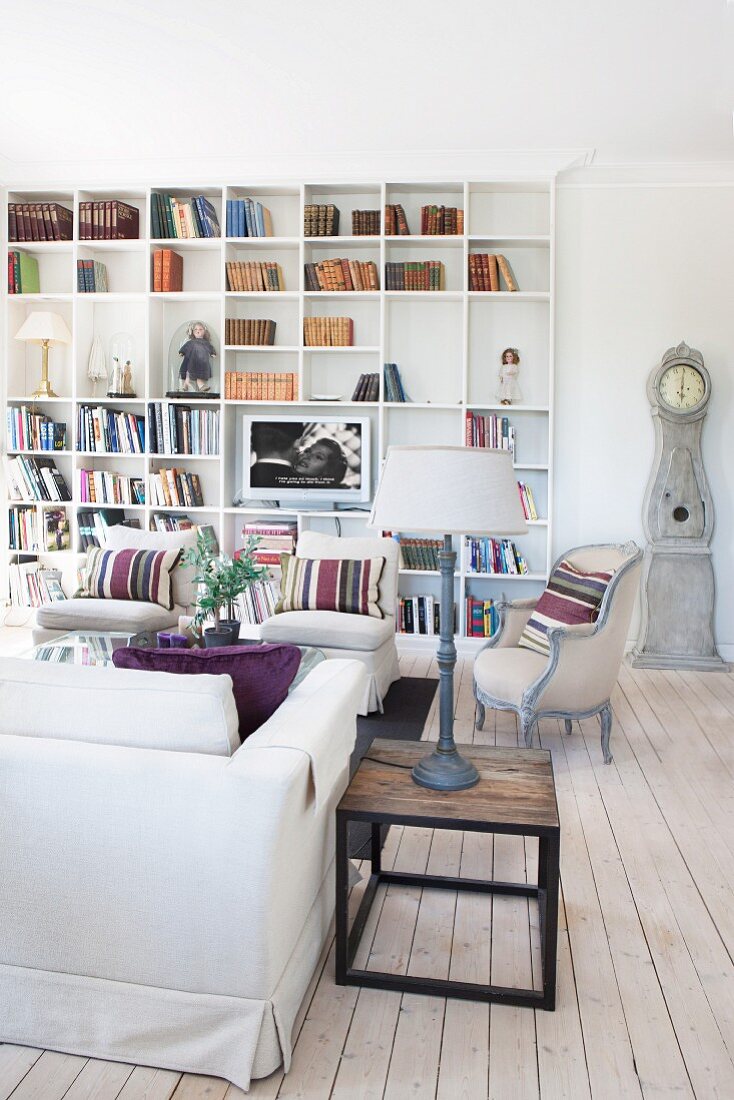 Table lamp on wooden side table and armchairs in front of fitted bookshelves