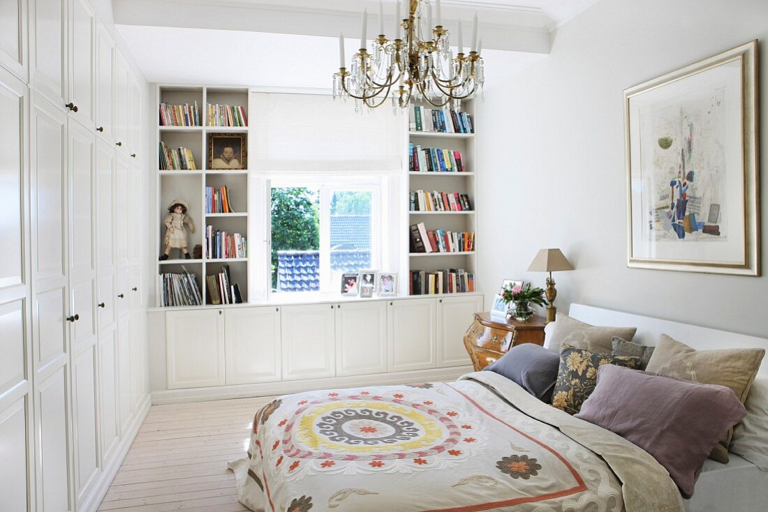 Double bed with patterned bedspread and many scatter cushions in rustic bedroom with custom wardrobes and white shelving