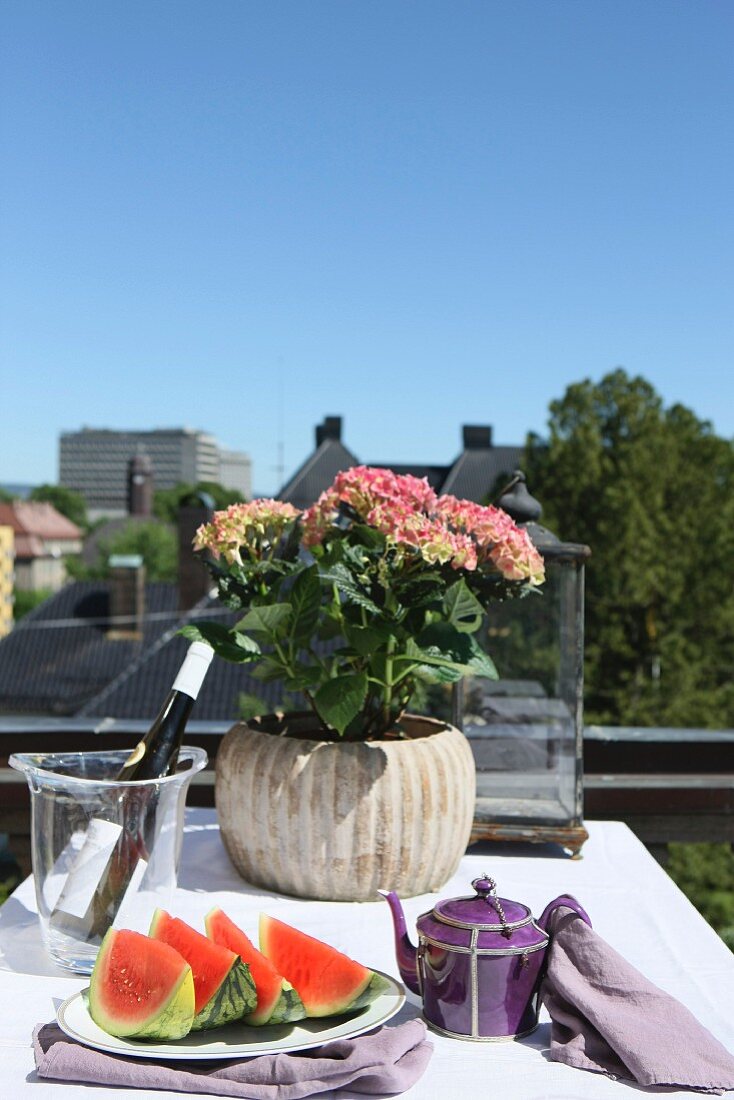 Slices of melon on plate and potted hydrangea on table with white tablecloth on balcony