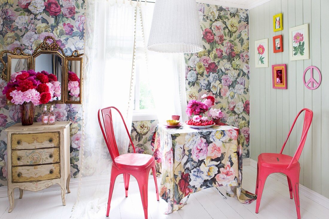 Floral wallpaper, matching tablecloth and pink, retro, metal chairs; peonies on vintage cabinet and vanity mirror to one side