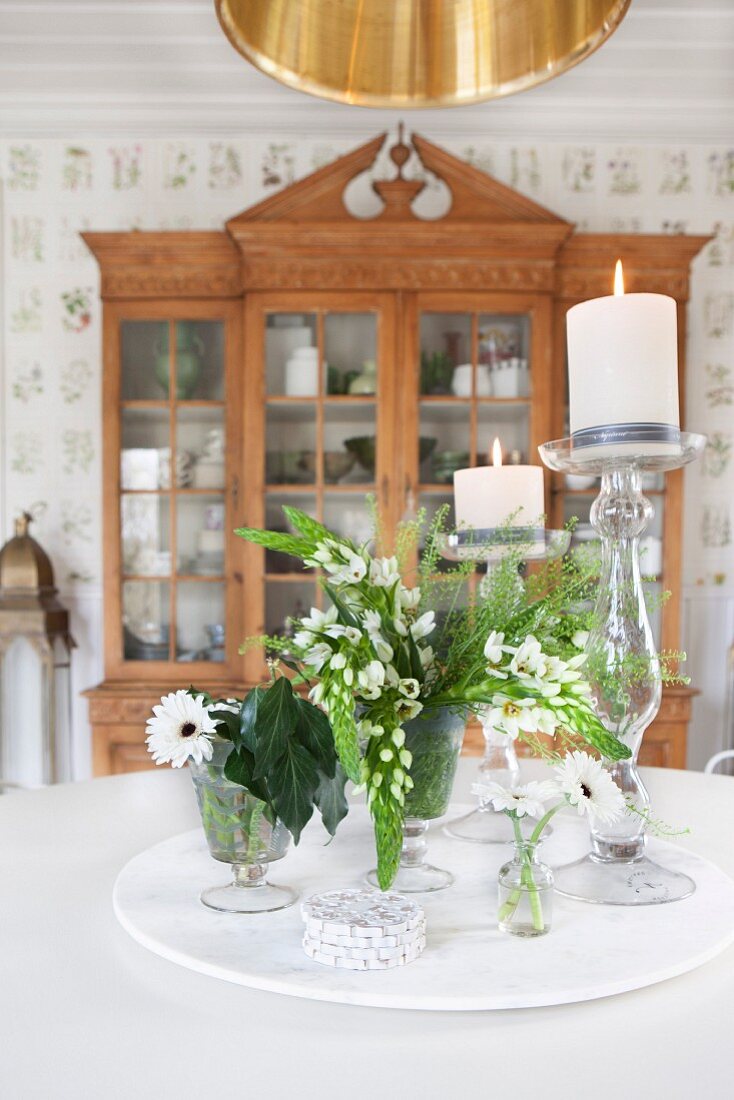 weiße Blumen und Kerzenhalter mit brennenden Kerzen auf Tisch, im Hintergrund antike Vitrine