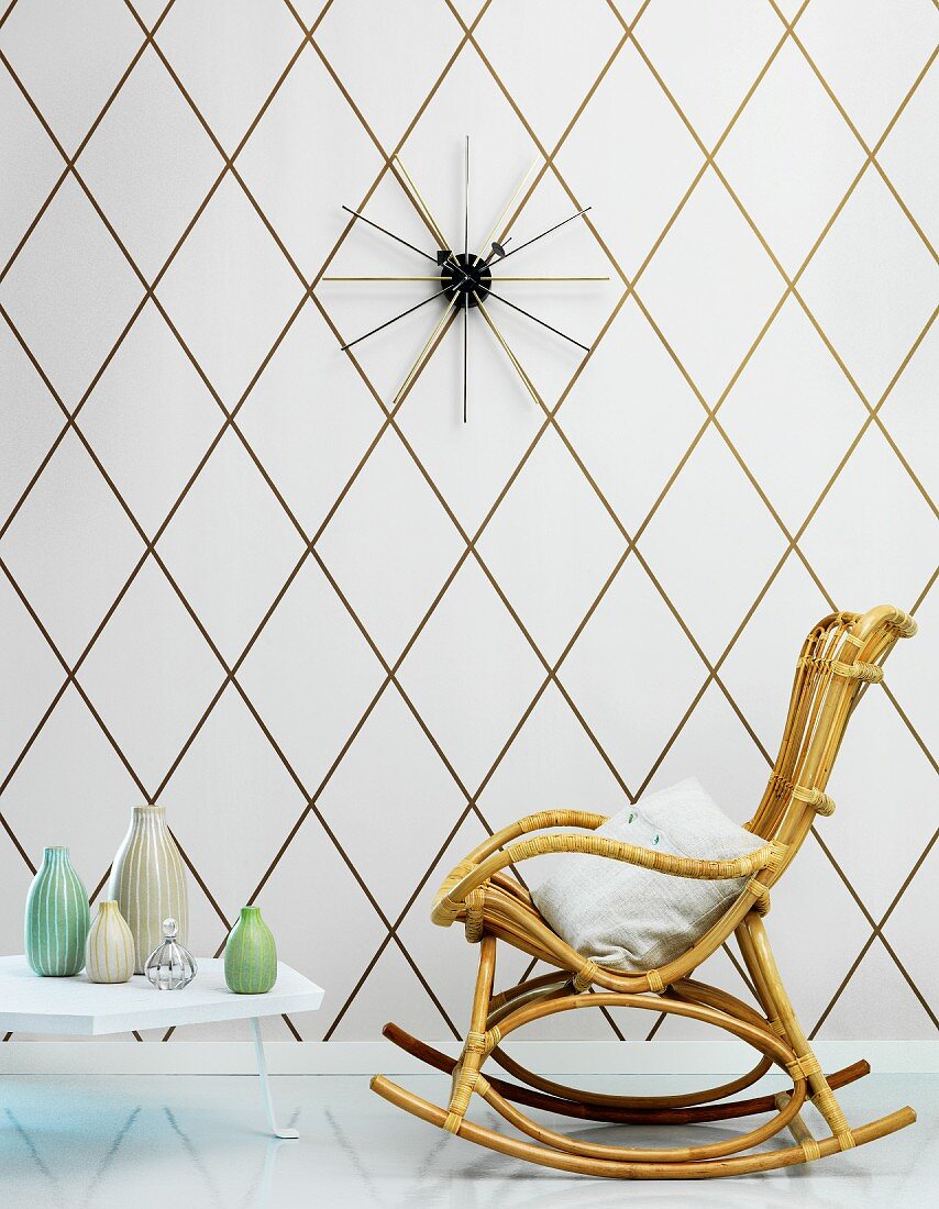 Schaukelstuhl aus Bambus und Bodentisch mit Vasensammlung vor Tapete mit geometrischem Muster in Weiß und Gold