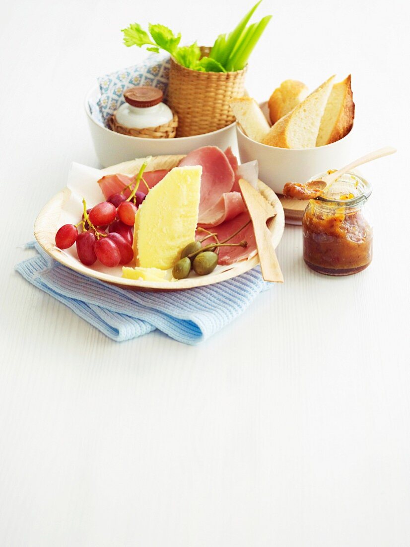 A small lunch plate with cheese, ham, bread, fruit and vegetables