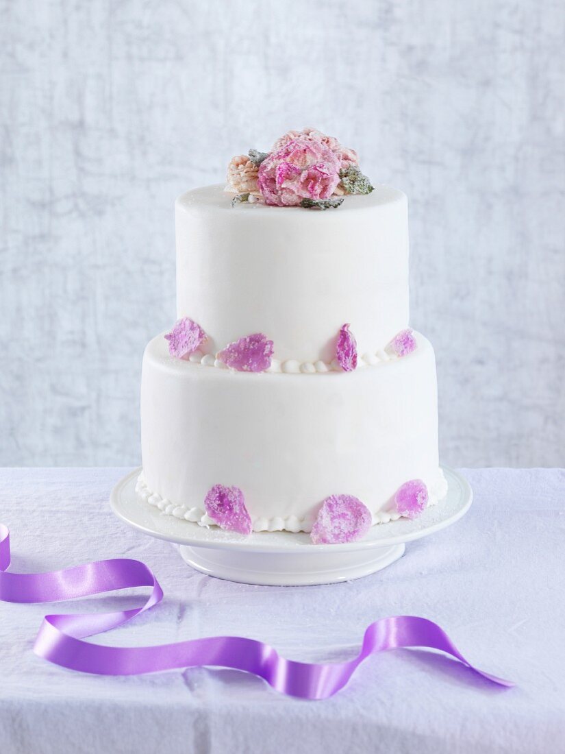 A two tier wedding cake decorated with candied flowers and petals