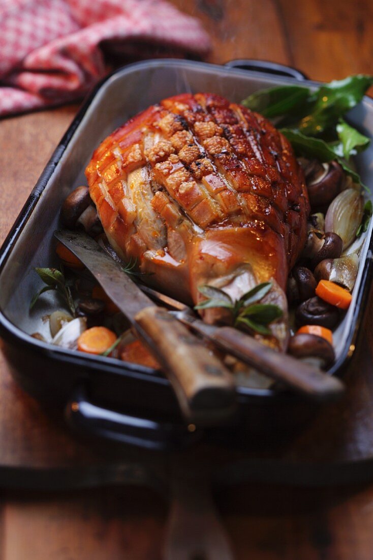 Studded pork knuckle with vegetables in a roasting tin