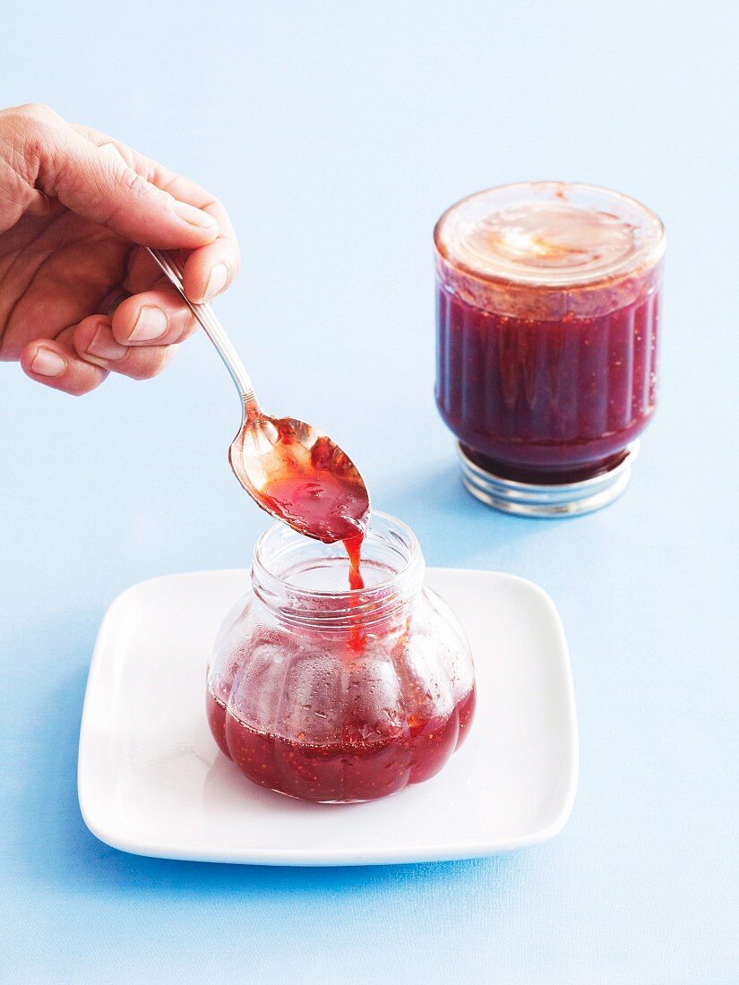 Strawberry jam being transferred into a jar