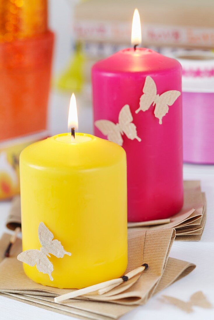 Brightly coloured candles on kraft paper coasters and decorated with punched paper butterflies