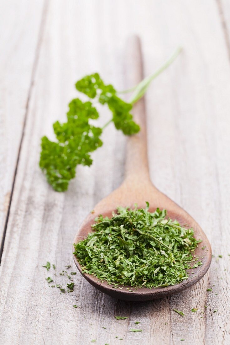 Dried parsley on a wooden spoon with a sprig of fresh parsley