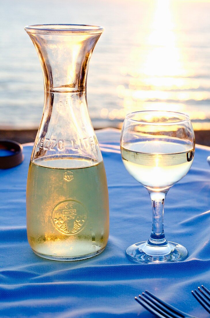 A carafe and a glass of white wine on a restaurant table with a sea view