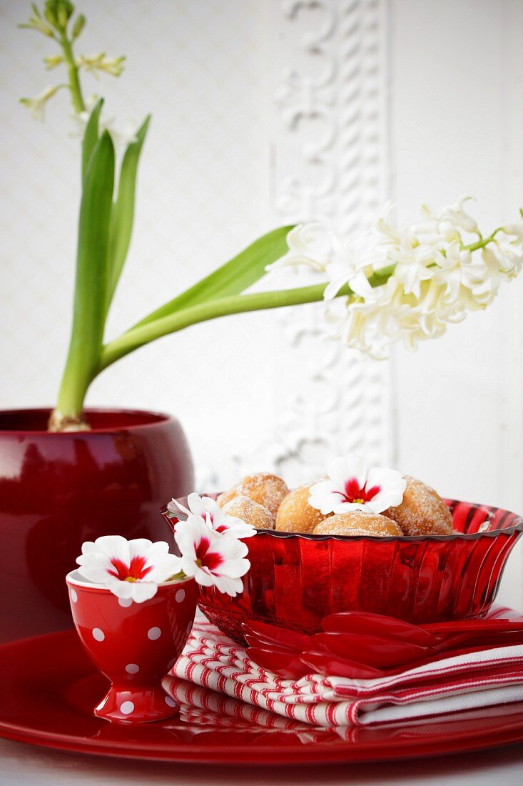 Miniature doughnuts in red glass bowl on table decorated with primula flowers & hyacinths
