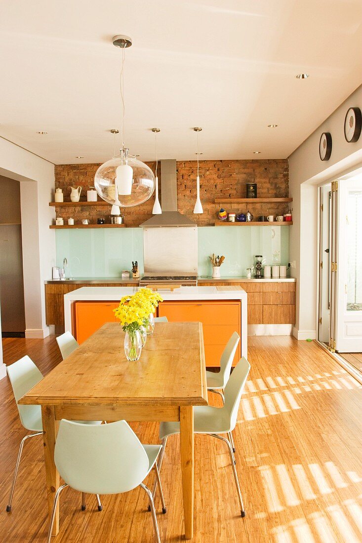 Modern shell chairs around solid wooden table in front of counter with orange drawer units in open-plan kitchen