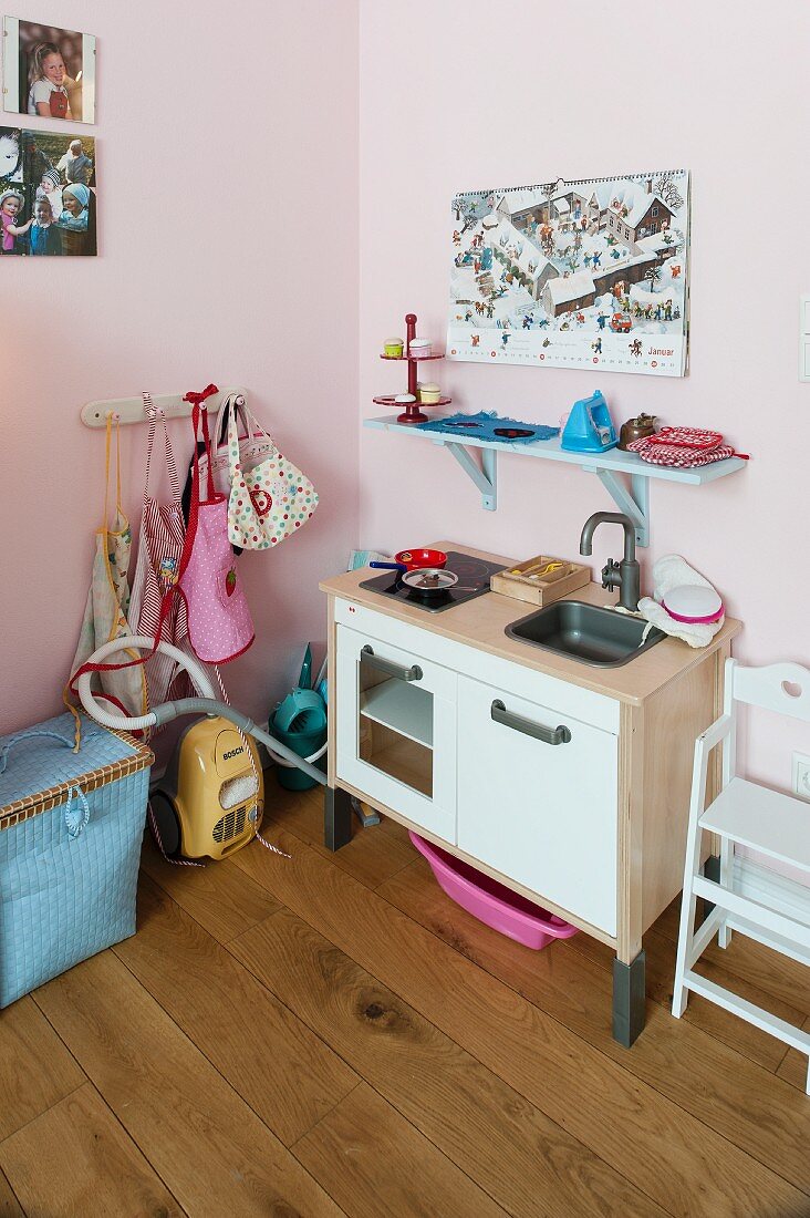 Toy kitchen and blue-painted bracket shelf on pink-painted wall in corner of child's bedroom