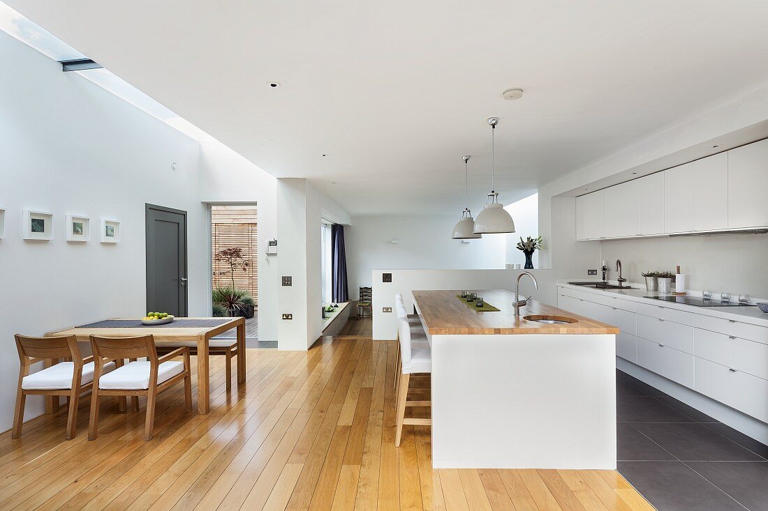 Open-plan designer kitchen - dining area with wooden table and chairs, island counter and fitted kitchen