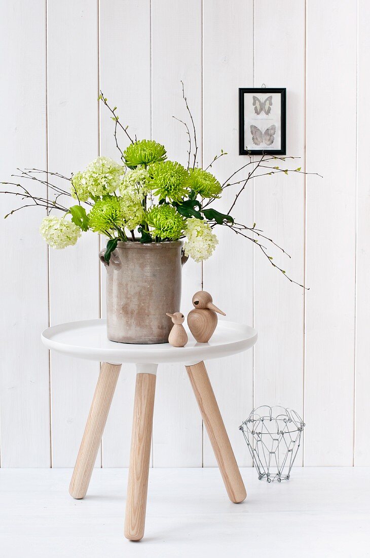 Chrysanthemums, viburnum and birch twigs in old stoneware jar on modern side table