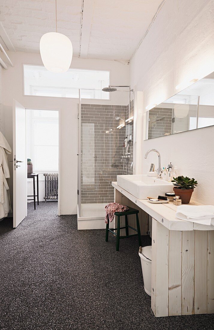 Selbstgebauter Waschtisch aus hellem Holz und Marmorkieselboden im Badezimmer einer Loftwohnung; Duschkabine mit Regendusche im Hintergrund