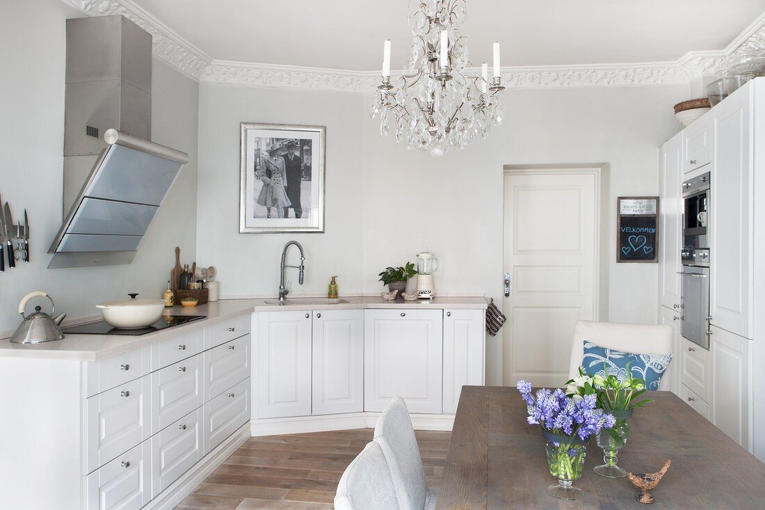 White fitted kitchen with chandelier and modern dining area in period apartment with stucco frieze