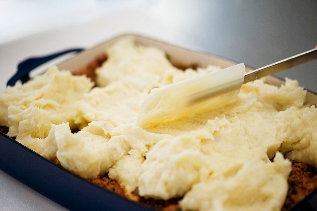 Mashed potatoes being added to a minced meat bake