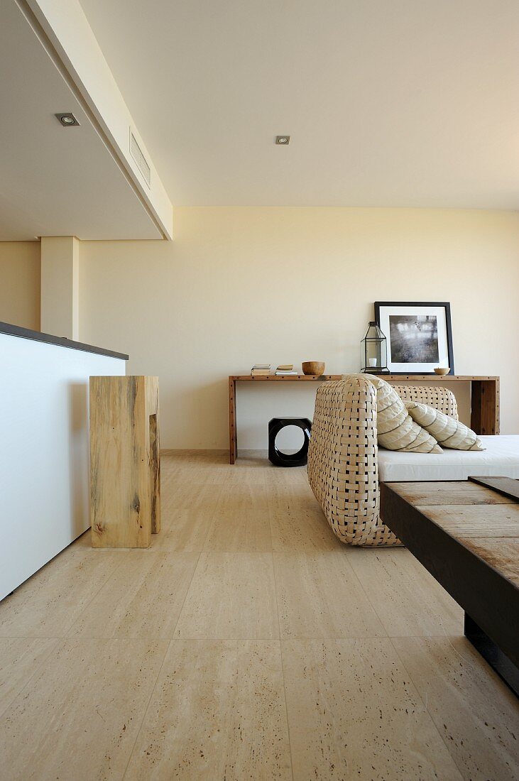 Open-plan interior with wood-block stool at kitchen counter and sofa with wicker frame; natural materials in pale shades