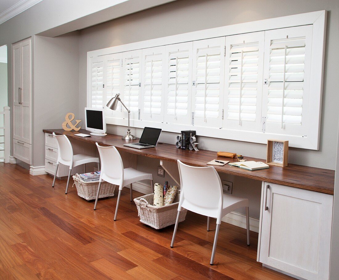 Office for three people in window niche in hallway; storage baskets on castors below long desk