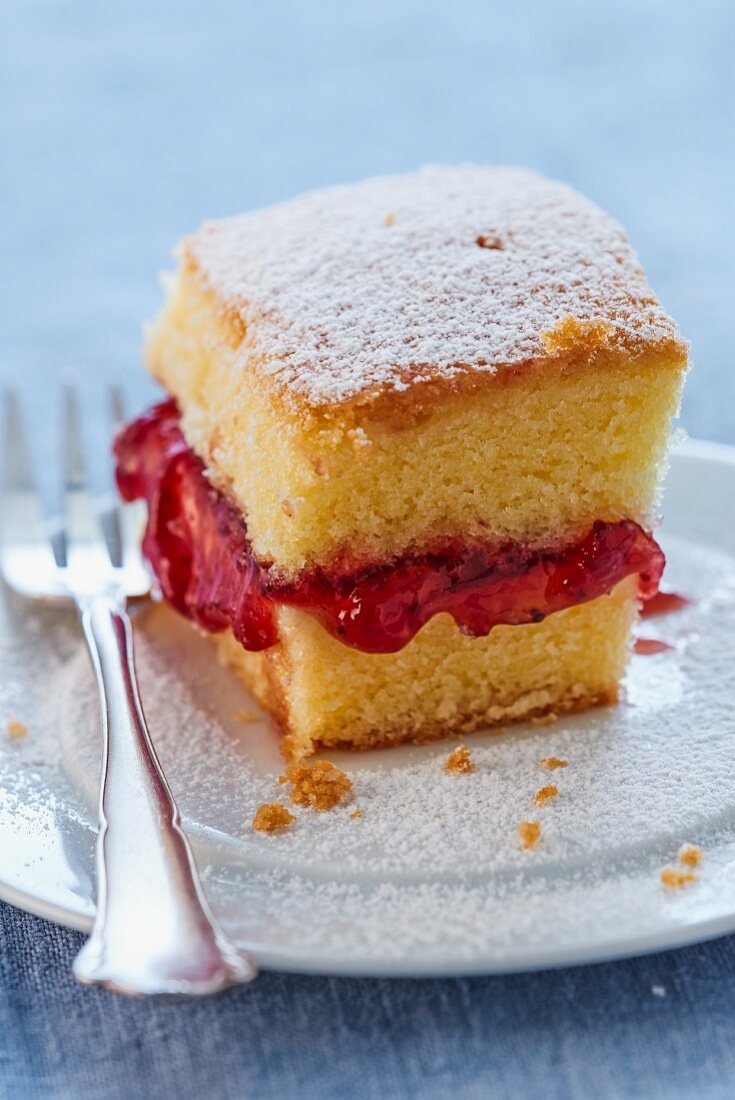 A slice of cake with strawberry jam and icing sugar