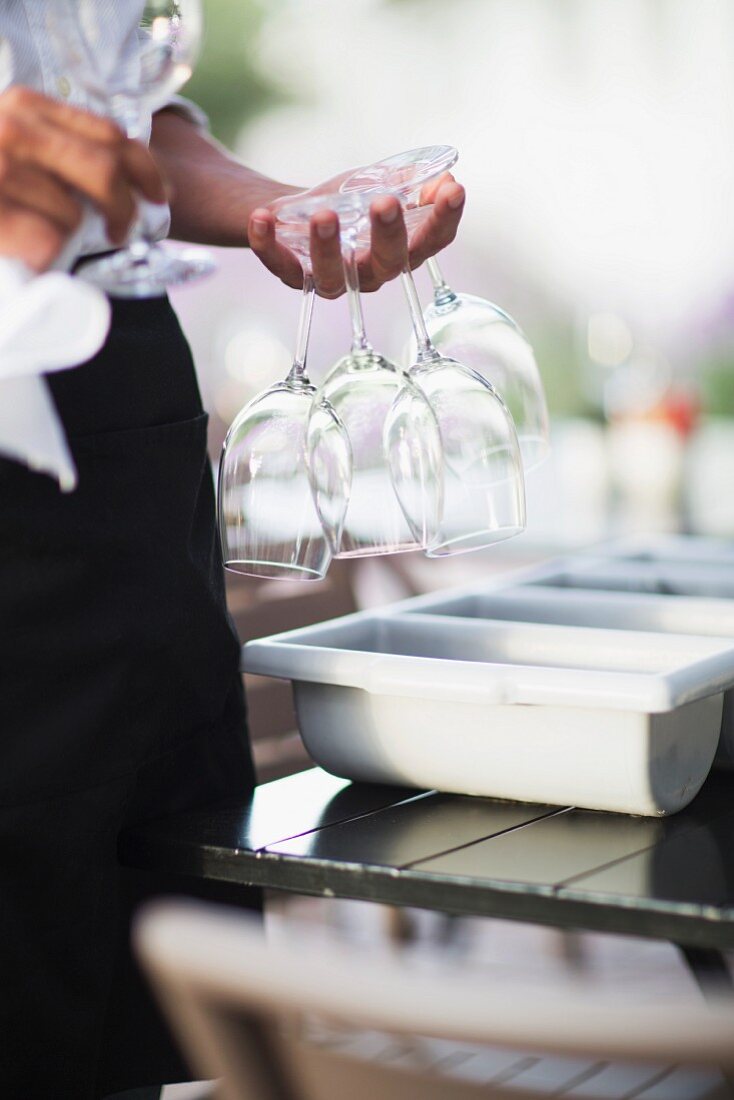 A waitress on the terrace of a restaurant holding wine glasses between her fingers