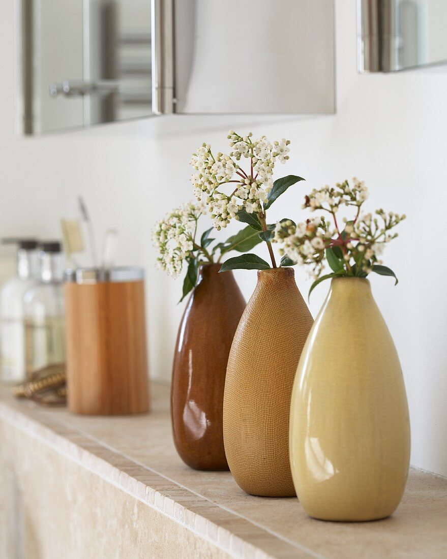 Flowering sprigs in row of three ceramic vases in various shades of brown