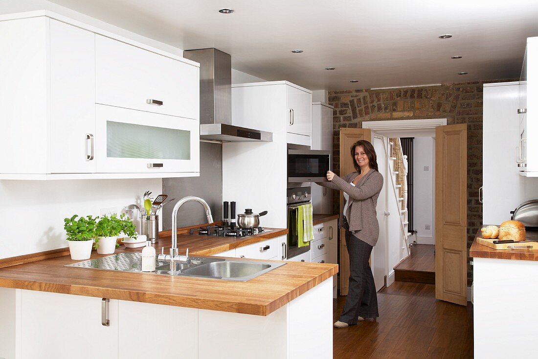 Modern, white fitted kitchens with wooden work surfaces; woman opening microwave