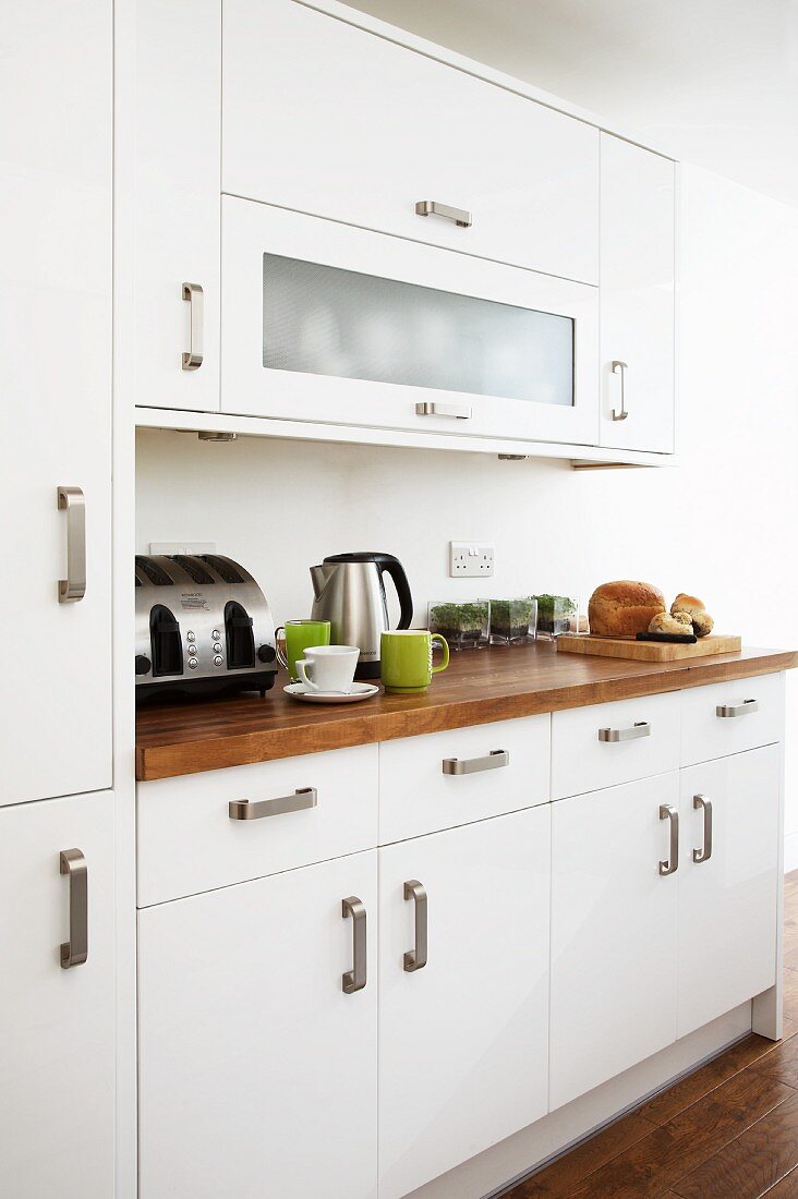 White fronts with robust, U-shaped handles and exotic wood work surface in modern fitted kitchen