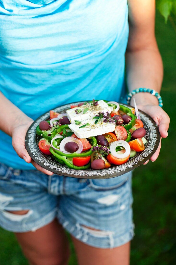 Frau hält Teller mit Griechischem Salat