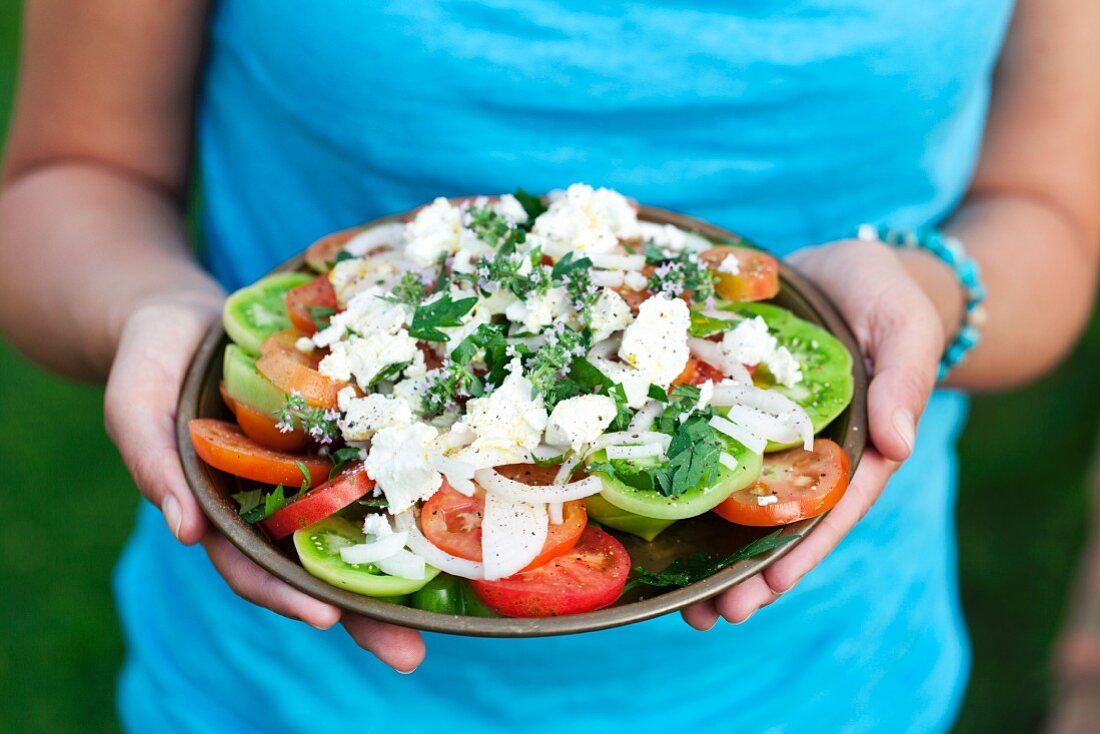 A woman holding a plate of Greek salad
