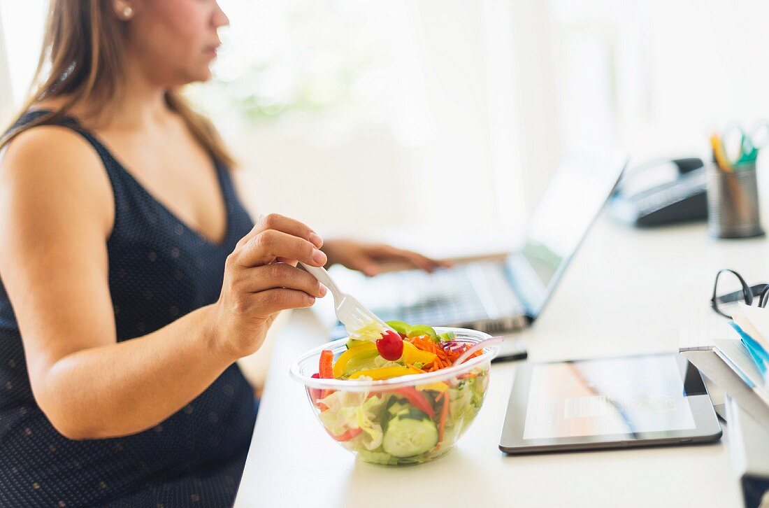A woman working in a home office and eating salad