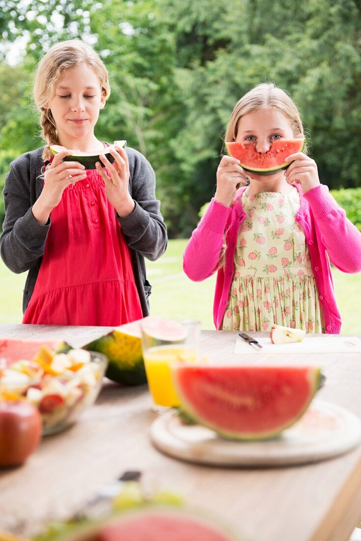 Two sisters on a terrace eating and holding watermelon wedges