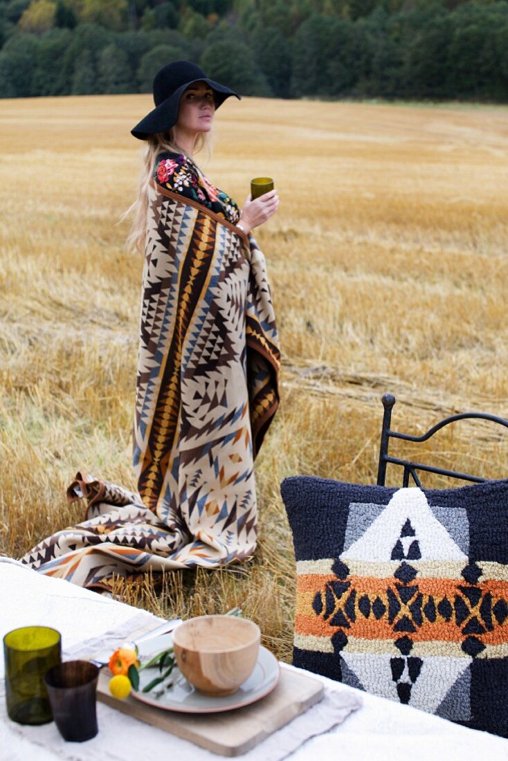 Young woman wearing hat and draped in blanket in stubbly field