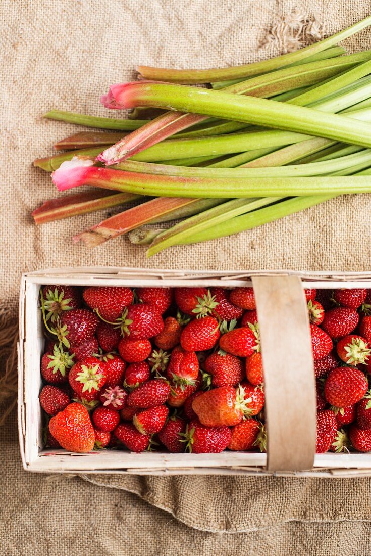 Strawberries in a wooden basket next to rhubarb