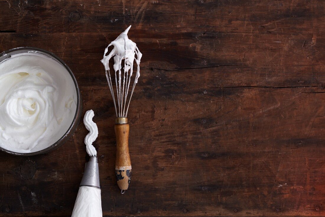 Beaten egg white in a bowl, a piping bag and on a whisk