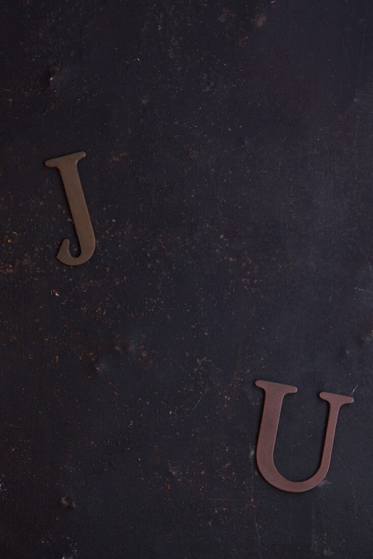 J und U als Papierbuchstaben auf dunklem Untergrund