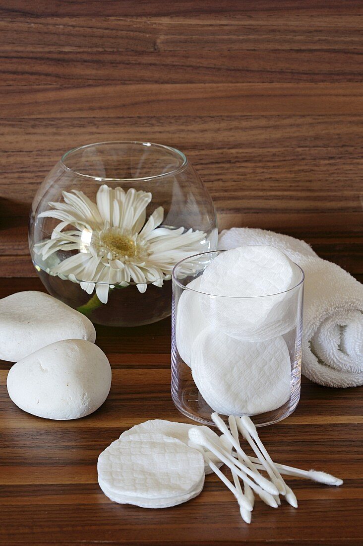 Cotton pads, cotton buds, a hand towel and a white gerbera in a glass of water