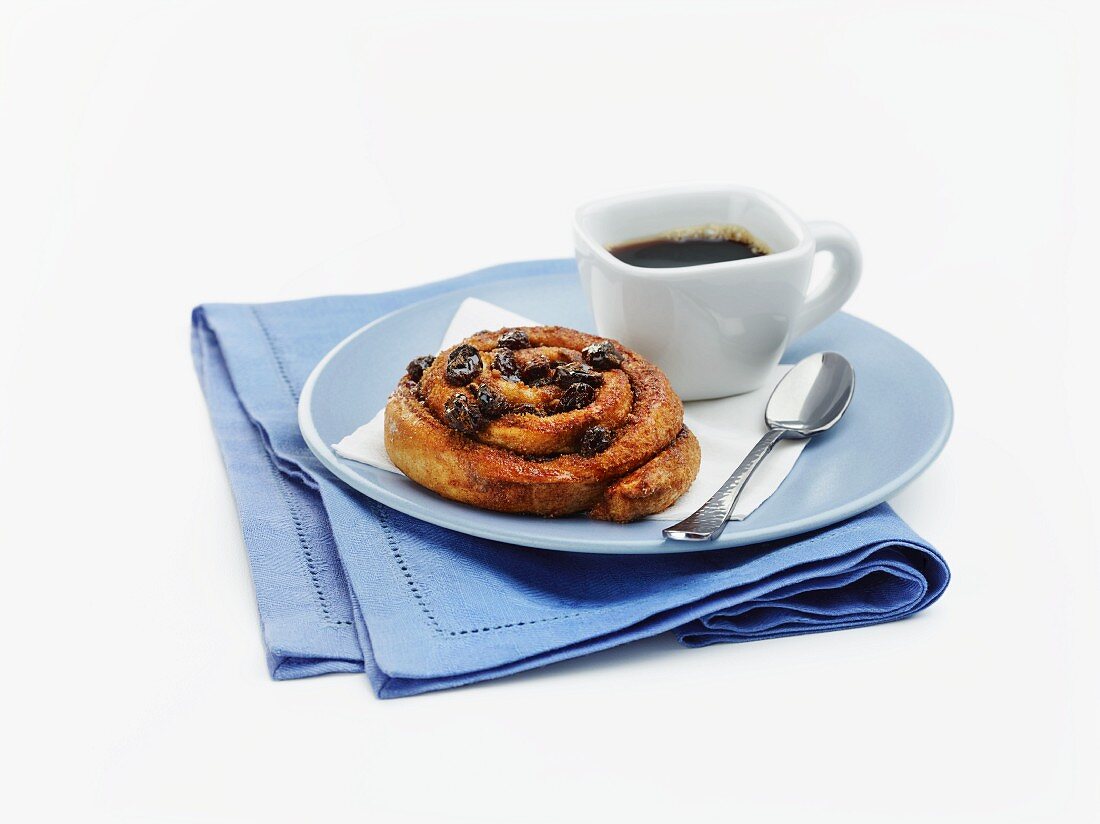 A wholemeal cinnamon bun with raisins served with coffee