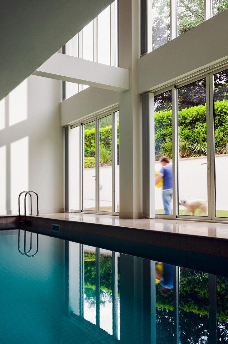 Indoor pool in contemporary house with double-height glass facade and view of garden