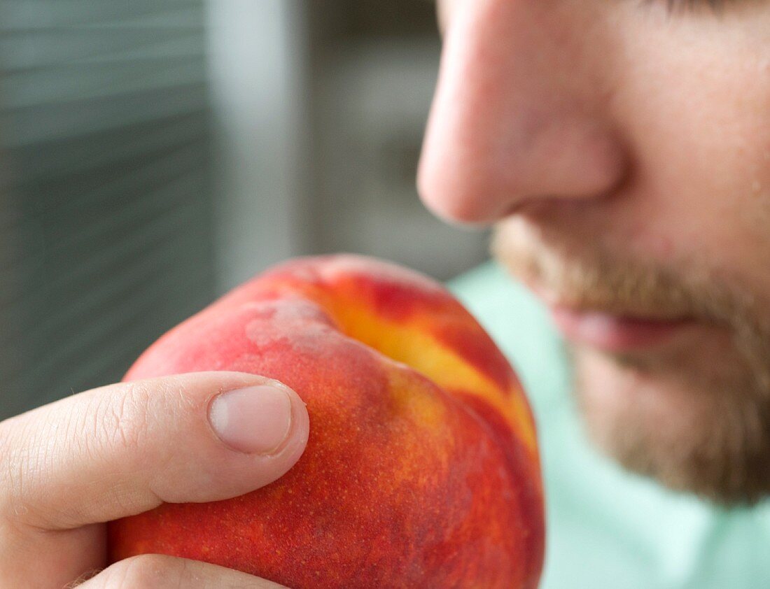 Mann riecht an einem Pfirsich