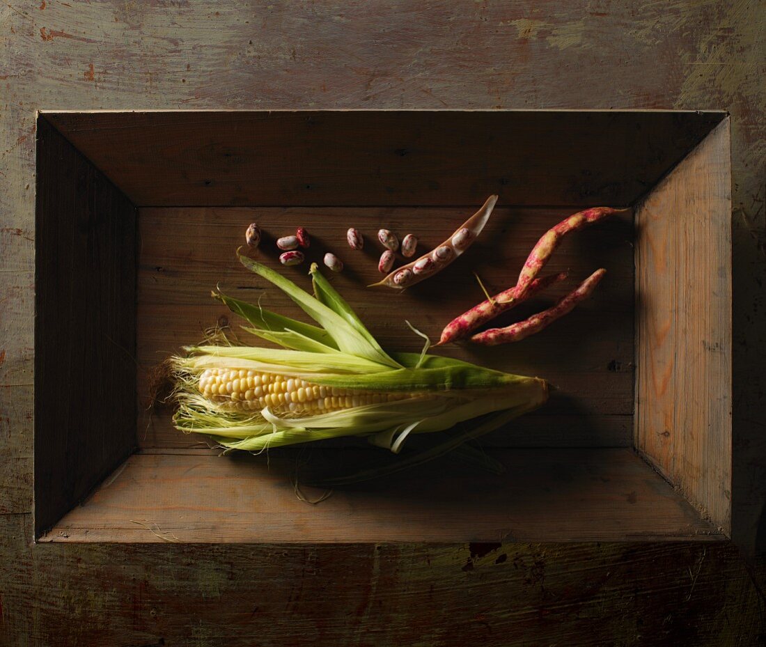 A corn cob and borlotti beans on a wooden tray
